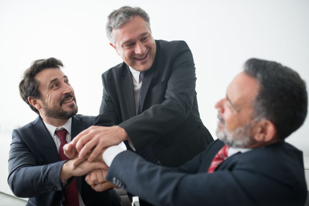 The Art of Drawing Readers In: Your attractive post title goes here Three businessmen in suits celebrating teamwork success indoors with handshake.